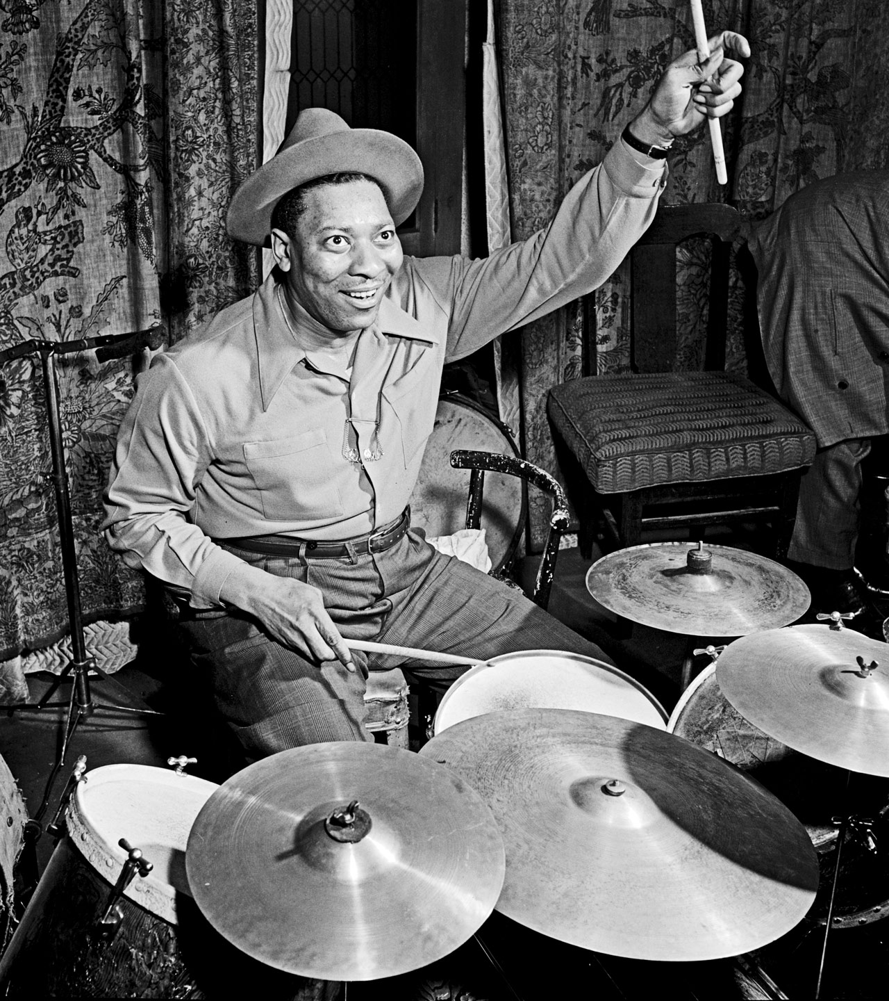 [Portrait of Sid Catlett, New York, N.Y., ca. Mar. 1947] — Caption from Down Beat: [from article] The shot of exuberant Sidney Catlett (who had just caught a flying drumstick) was taken during one of Louis Armstrong's last rehearsals before his Carnegie Hall concert. Can't report on Louis' recital since the Great One had not; at this writing, appeared. By the way, has it ever occurred to you, too, that Big Sid, whether at or away from his drums, gives an unsurpassed impression of tremendous physical power?